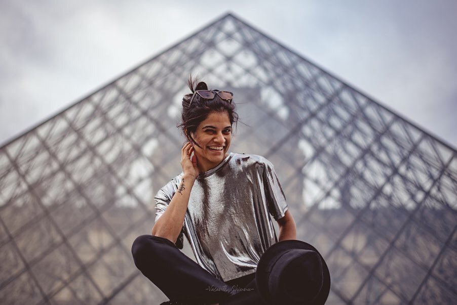 Maya Sundarakrishnan sitting pensive against a dark wall in a light-colored shirt.