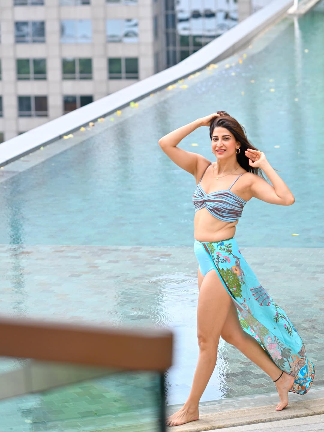 Aahana Kumra standing near water in a light-colored patterned fabric, looking at the camera.