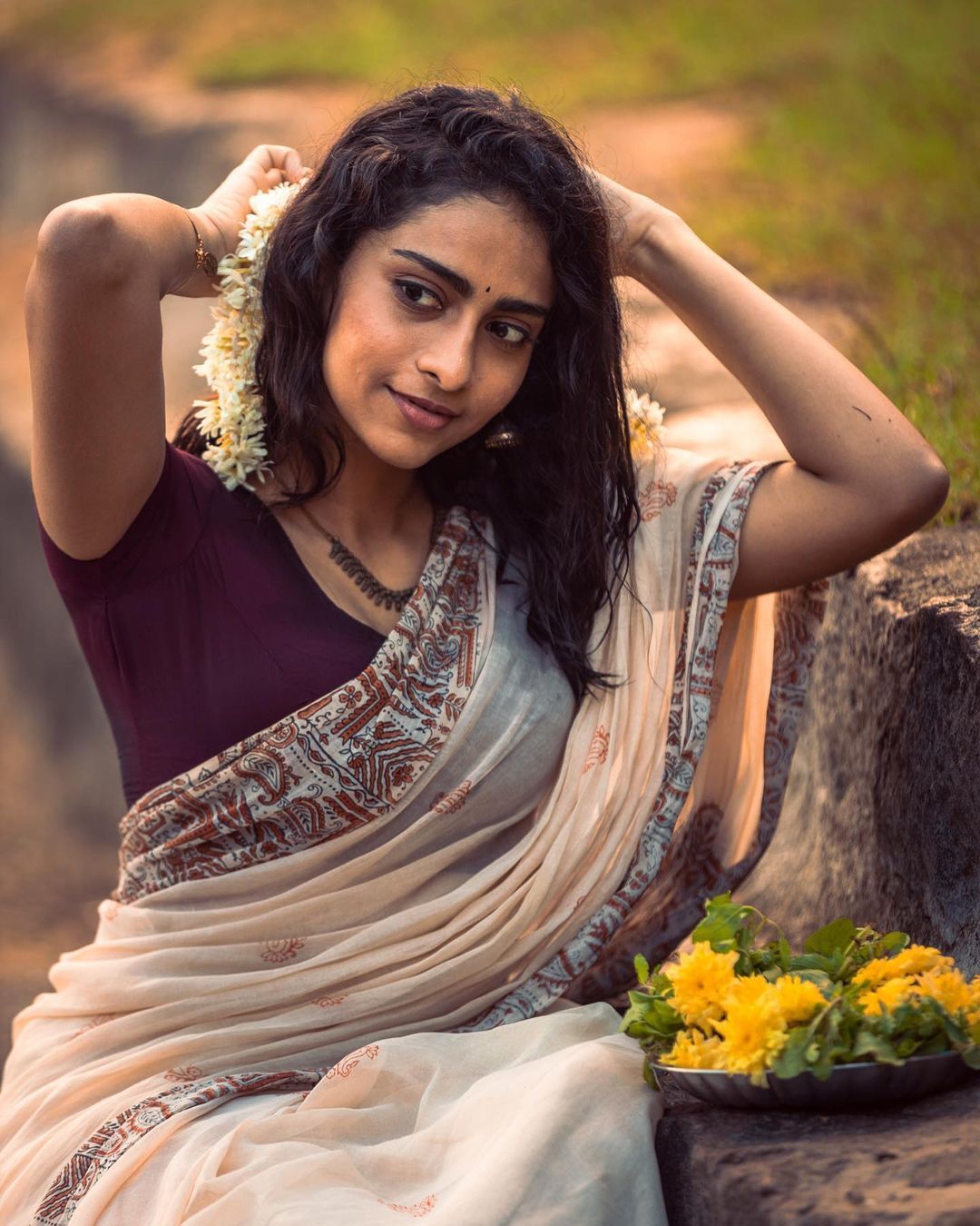 Abitha Venkat sitting against a plain wall wearing a light beige sleeveless top and light blue denim jeans.