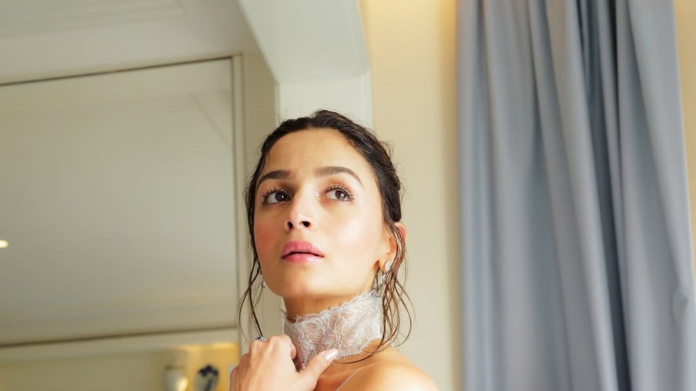 Alia Bhatt in a delicate white lace garment with intricate floral patterns and dangling earrings.