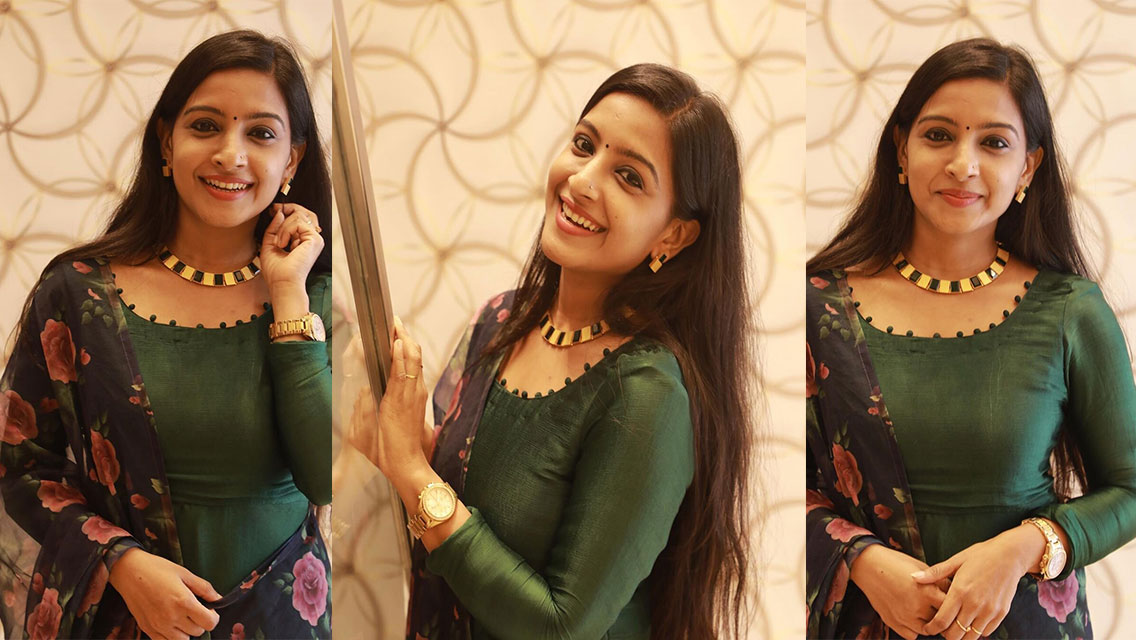 Alphy Panjikaran posing indoors wearing a deep green kurta and a floral patterned dupatta with gold jewelry.
