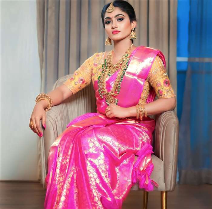 Anithra Nair is seated indoors wearing a striped kurta in gray and gold, with long dark hair and a gentle smile.