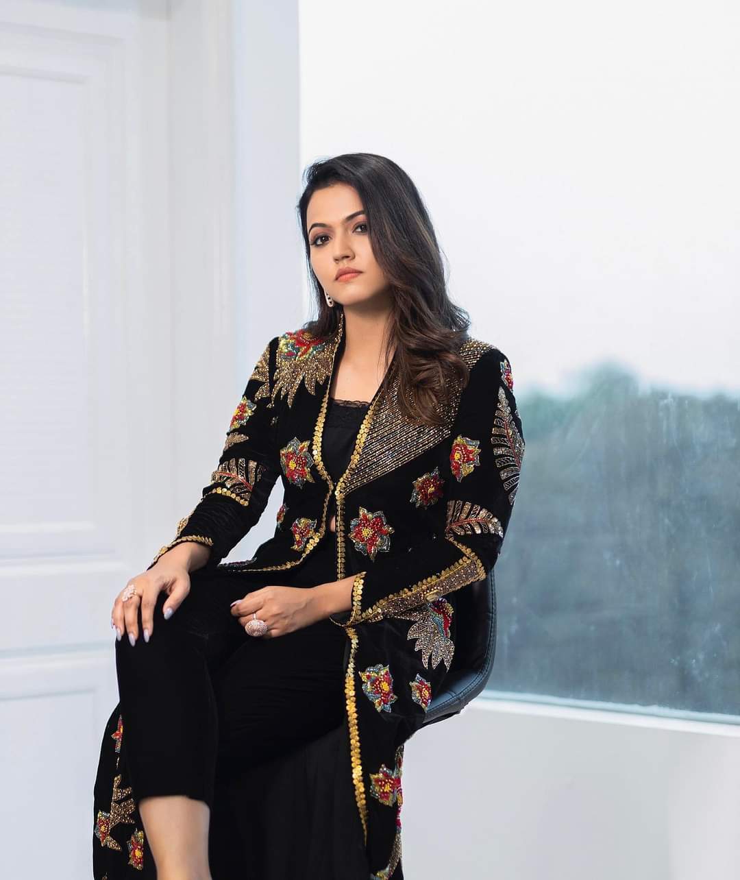 Aparna Das in a black sheer garment with dangling earrings and flowing dark hair against a patterned background.