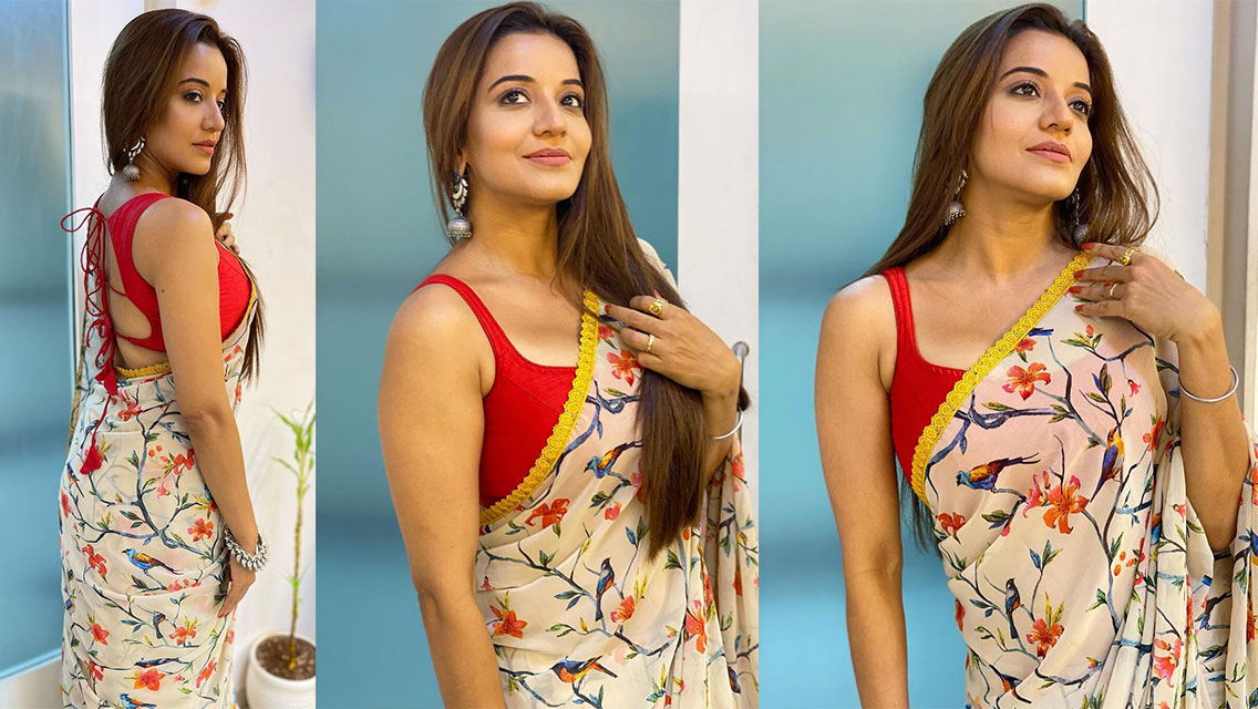 Asli Monalisa posing with a traditional floral saree in red, orange, green, and blue tones, featuring a golden border.