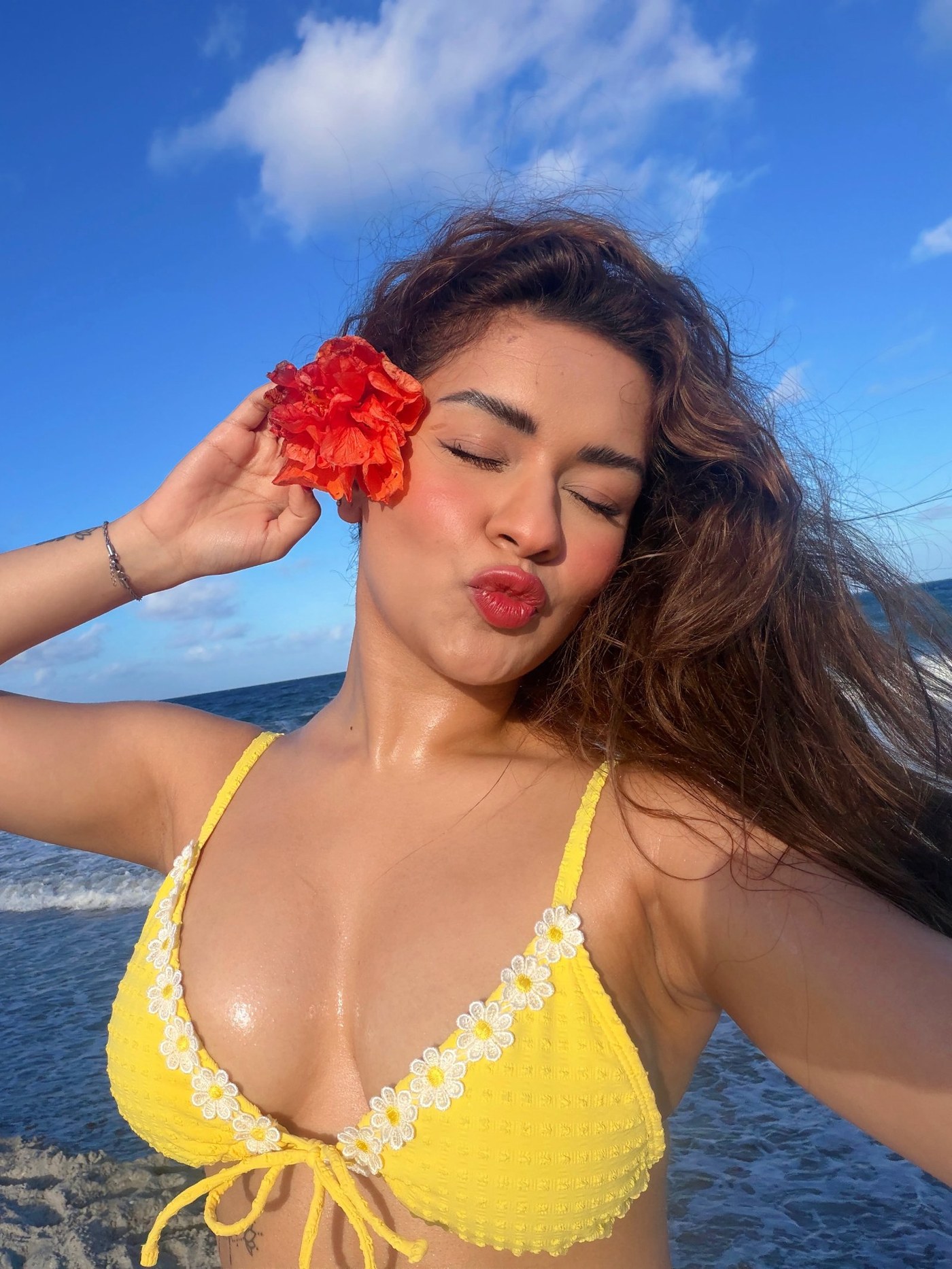 Avneet Kaur in a yellow bikini against a blue ocean backdrop.