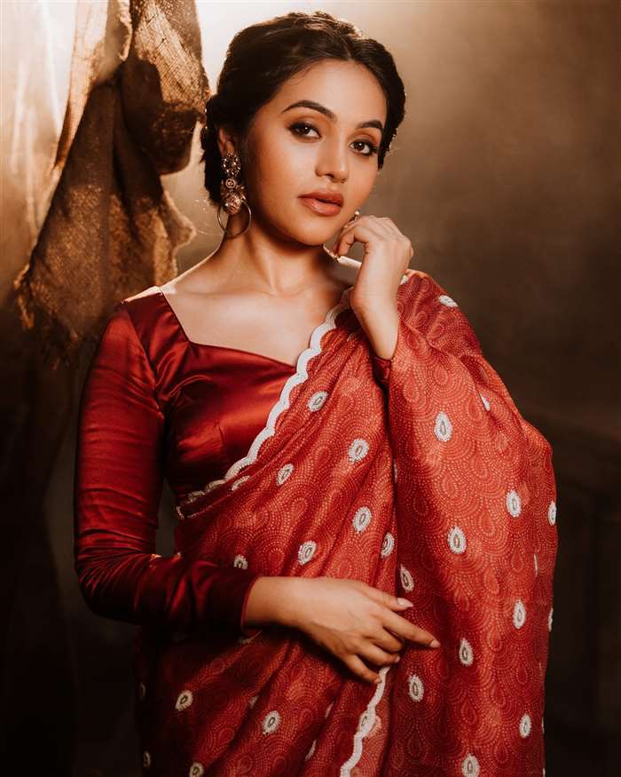 Bhavani Sre sitting on a wooden staircase indoors wearing a maroon top and cream trousers.