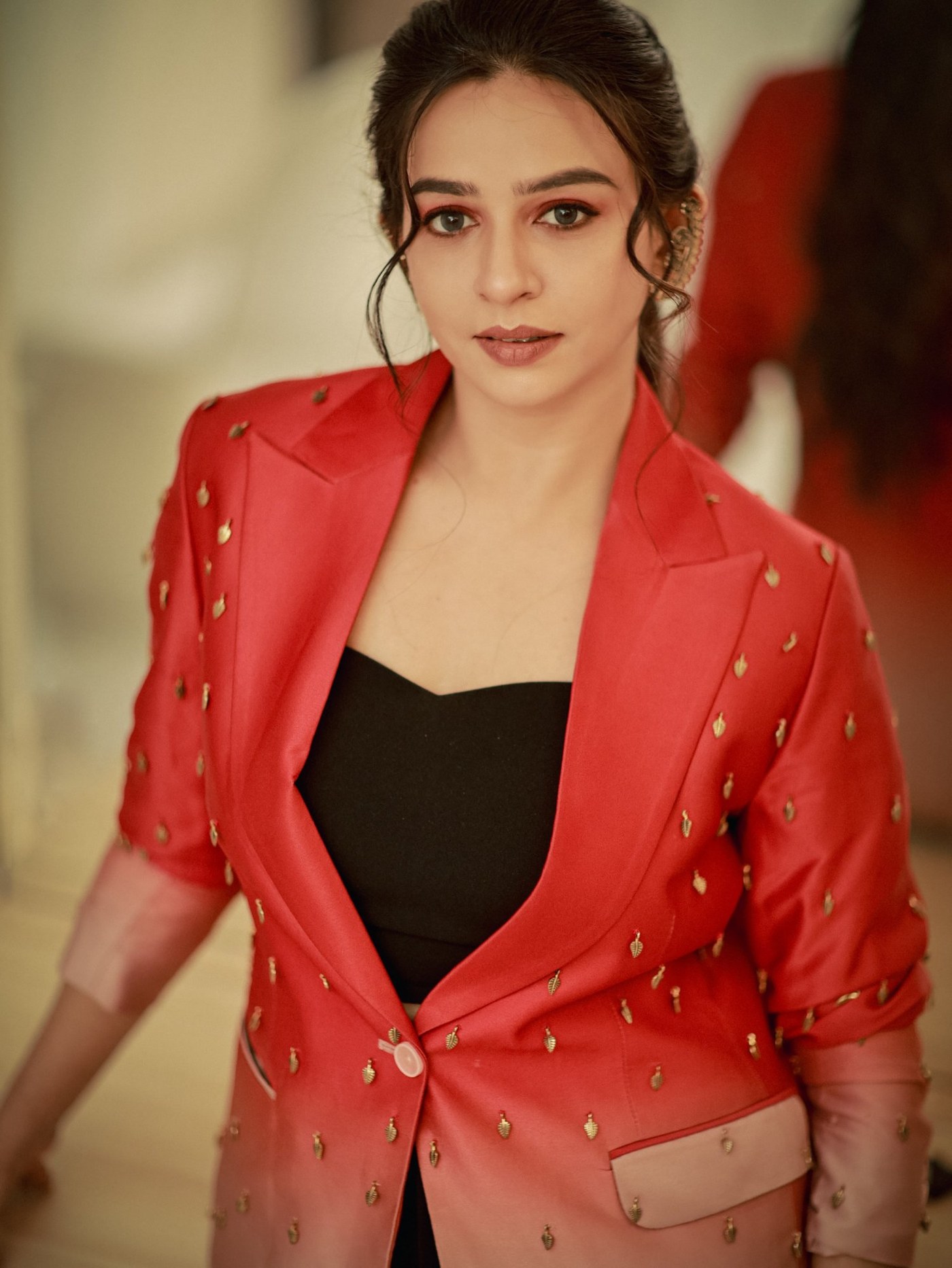 Divya Ganesan showcases sophisticated style in a vibrant red tailored blazer paired with sleek black trousers.