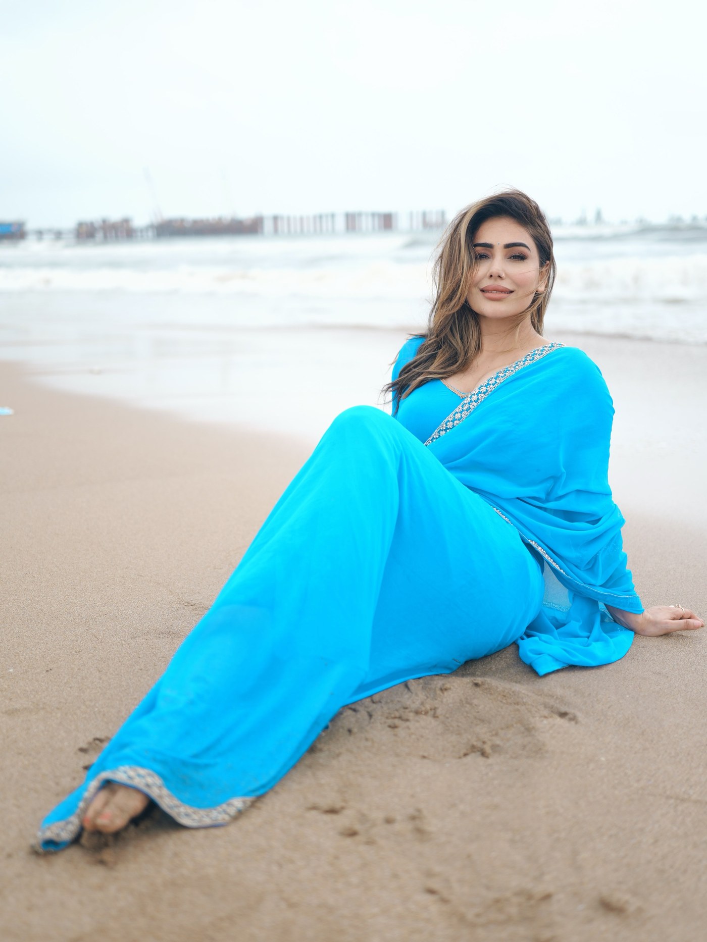 Kangana Sharma is seen in a vibrant blue ethnic ensemble against a soft, diffused background while posing confidently.