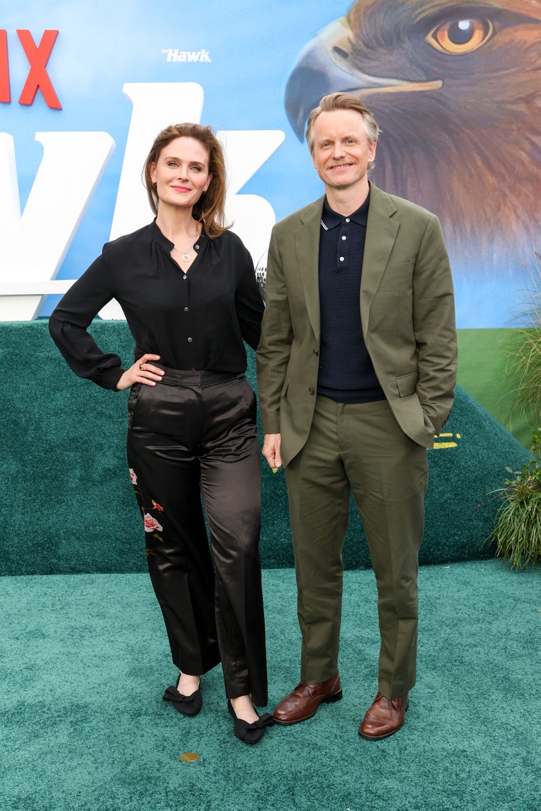 Emily Deschanel stands beside a companion at an indoor event against a backdrop of graphic signage.