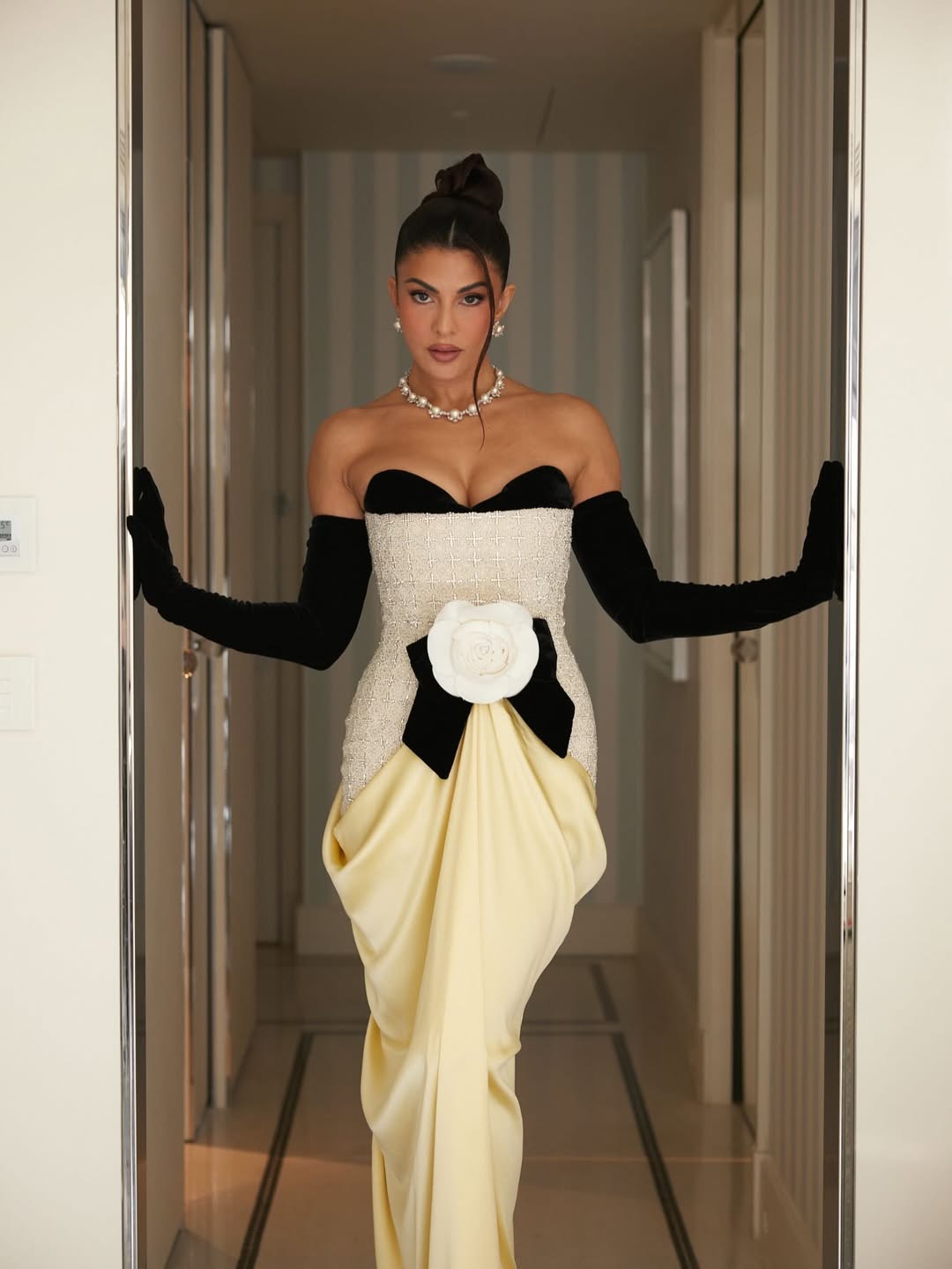 Jacqueline Fernandez posing on an ornate staircase railing in a grand interior setting.