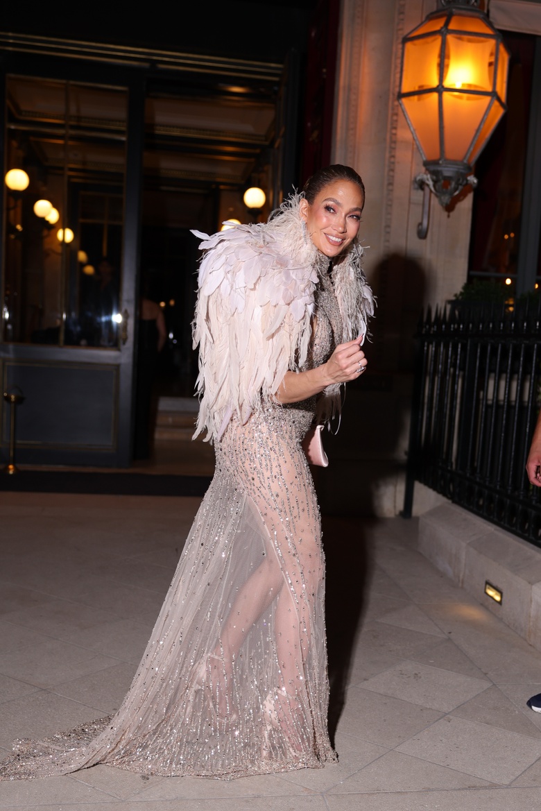 Jennifer Lopez stands outdoors at night, showcasing a voluminous feathered stole and pale clutch.