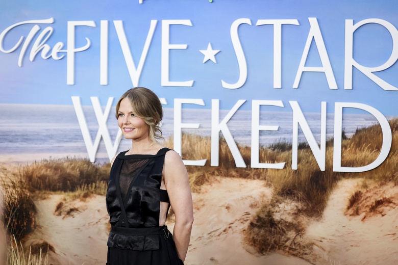 Jennifer Morrison is pictured outdoors against a vibrant blue backdrop while wearing a sophisticated black gown.