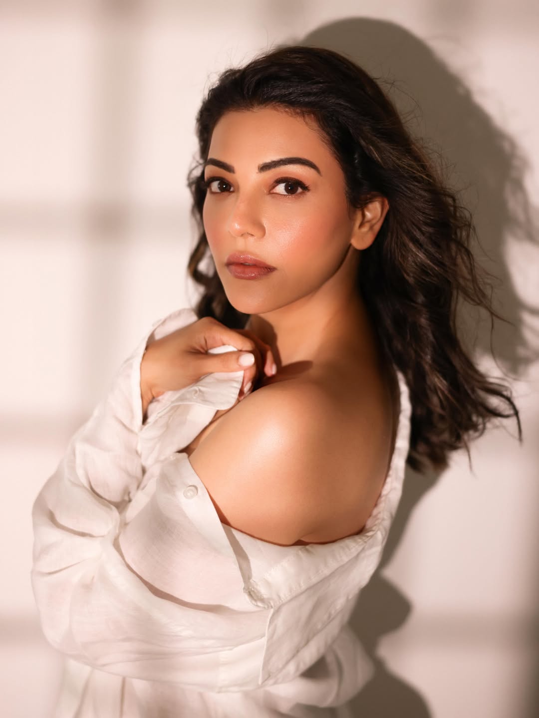 Kajal Aggarwal holding a large bouquet of white flowers while wearing a white shirt and blue jeans.