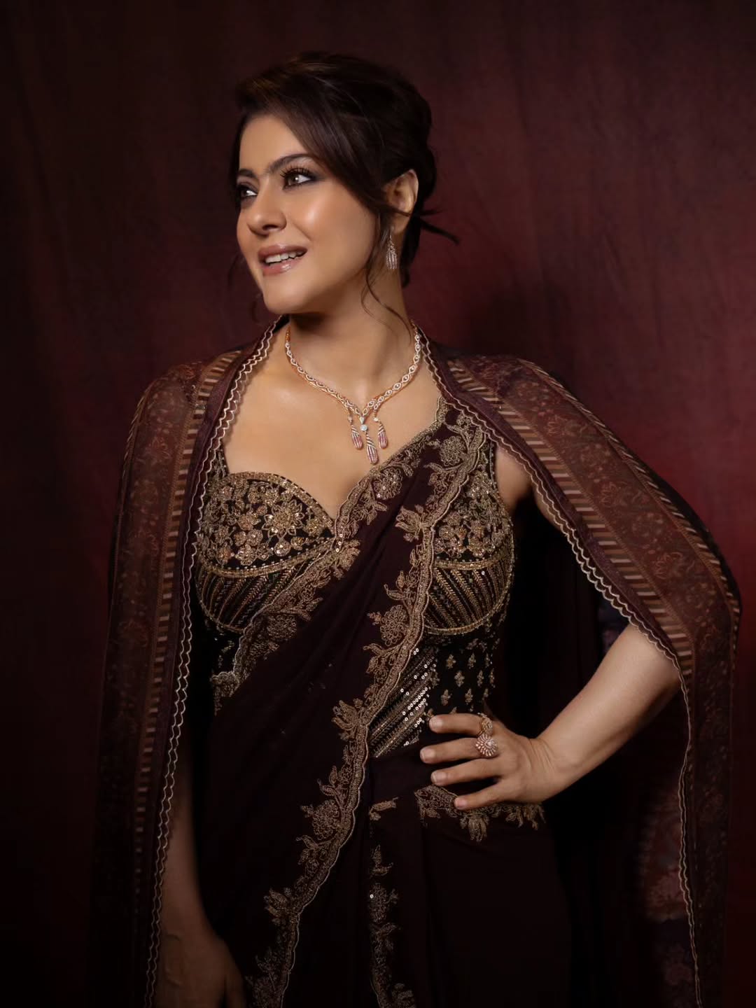 Kajol in a close-up portrait wearing a maroon outfit with gold embroidery and intricate jewelry.