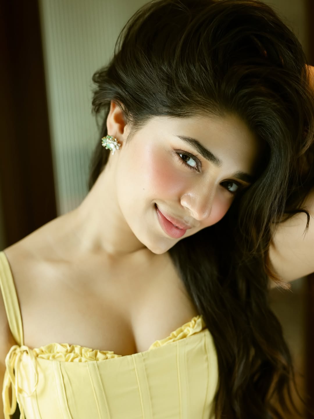 Krithi Shetty posing outdoors, leaning against a dark railing and draped in a flowing pink garment.