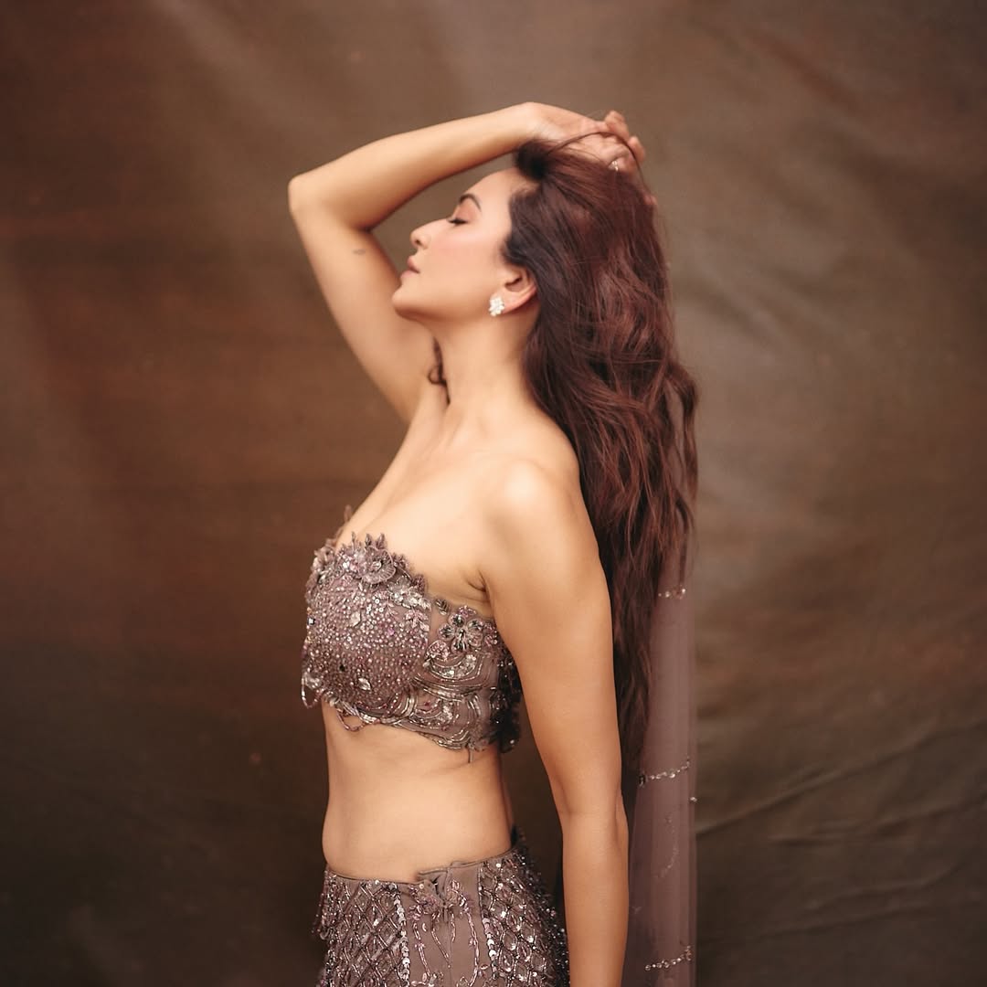 Kriti Kharbanda is seated in a brown leather armchair wearing a heavily embellished, sequined outfit.