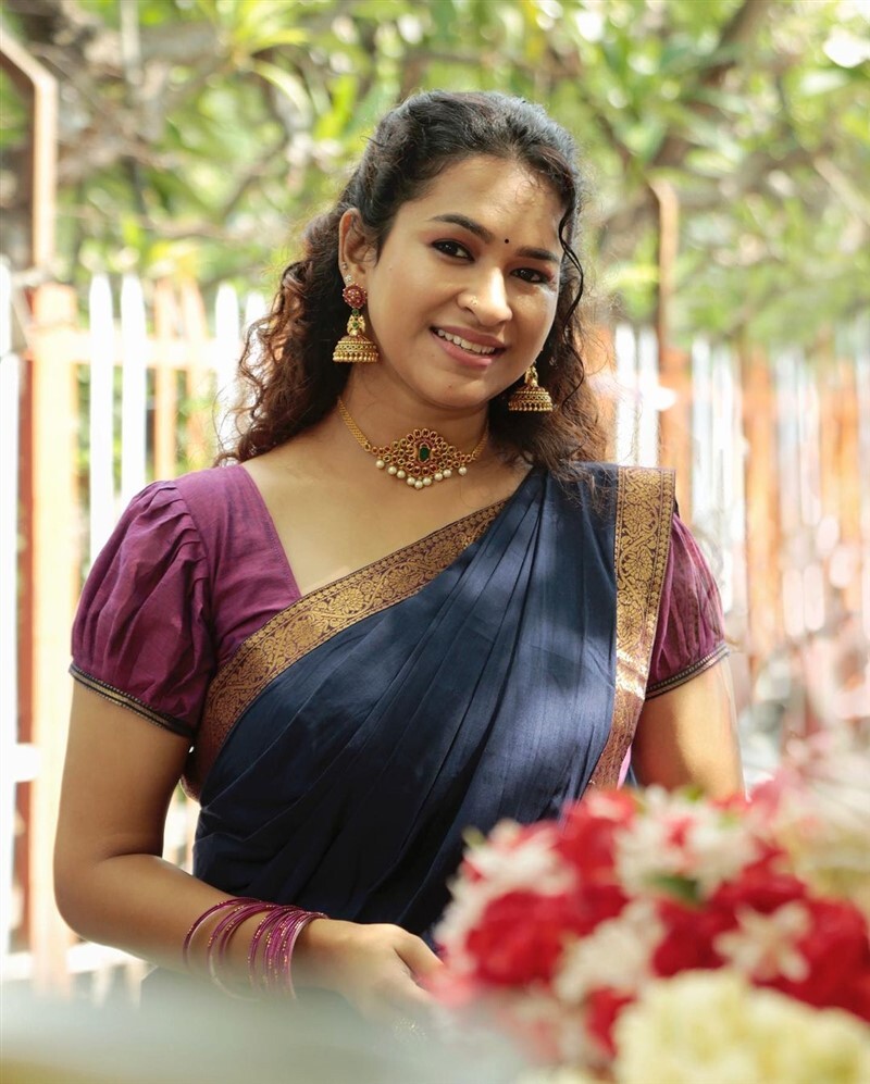 Meesha Ghoshal posing indoors in a black patterned top and black wide-leg trousers with flip-flops.