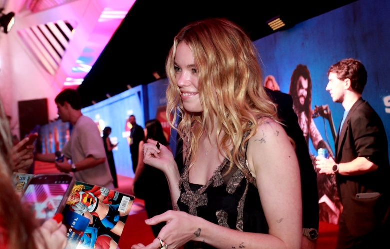 Milly Alcock posing elegantly in a vibrant red carpet setting during an event.