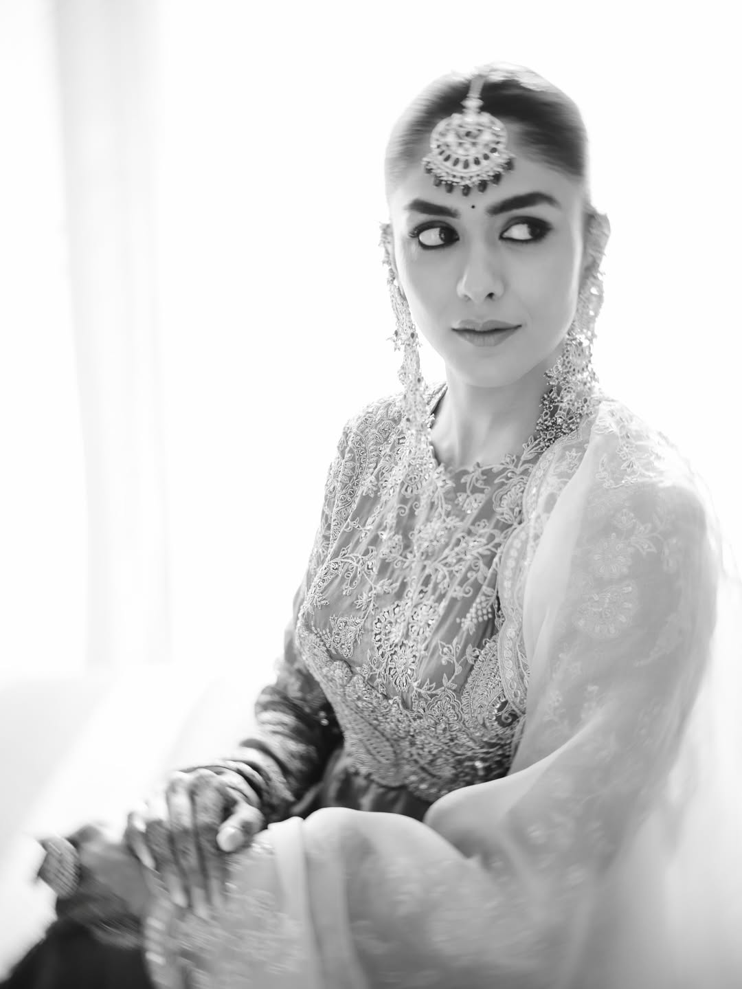 Mrunal Thakur draped in a vibrant orange and ivory ensemble with gold embroidery and elaborate earrings.