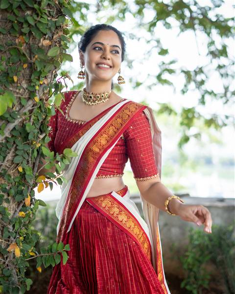 Bindu Madhavi poses gracefully outdoors wearing a stunning red, orange, and white patterned saree ensemble.