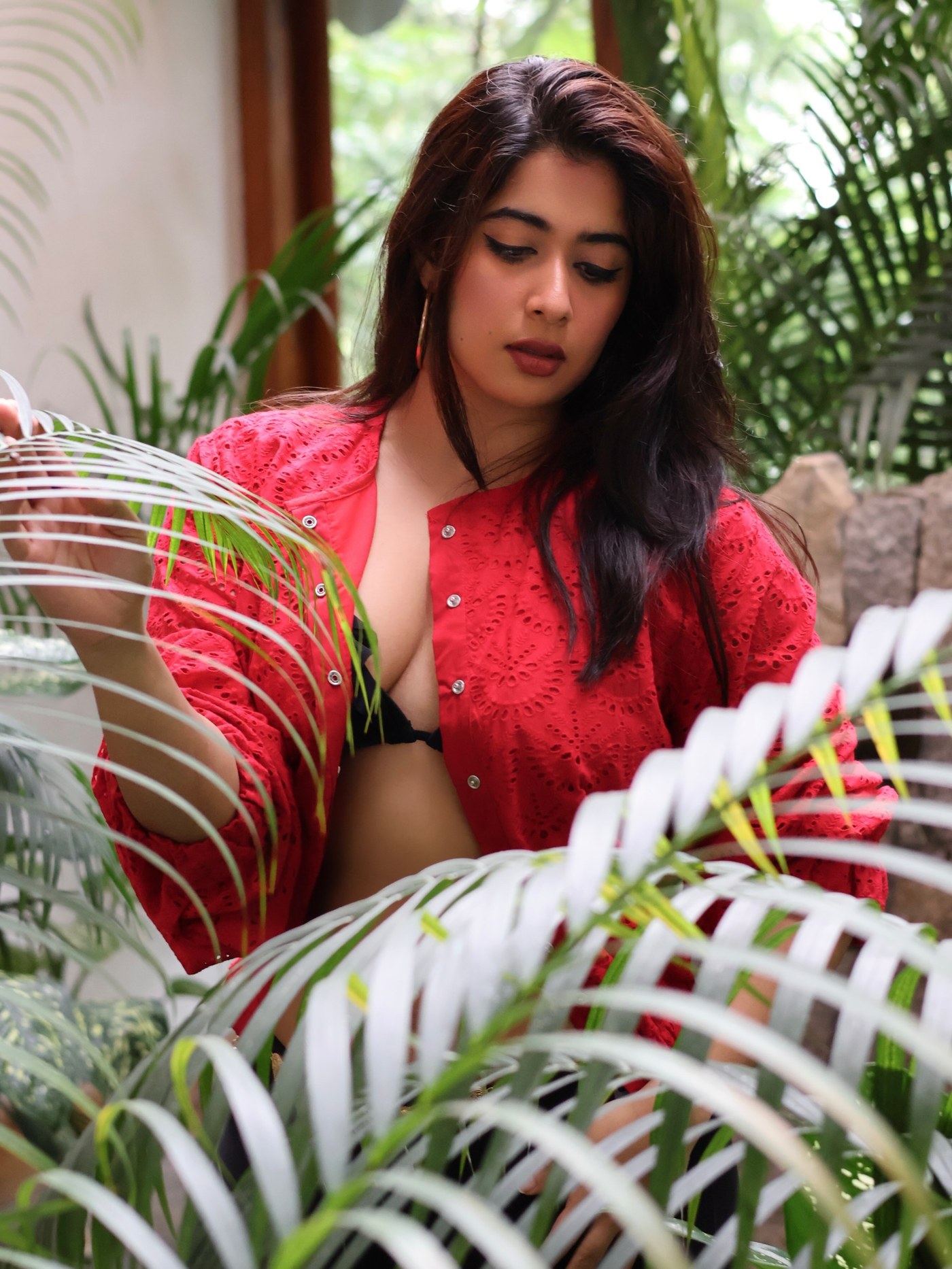 Nikita Sharma poses confidently in a vibrant fiery red statement jacket against a backdrop of natural greenery.