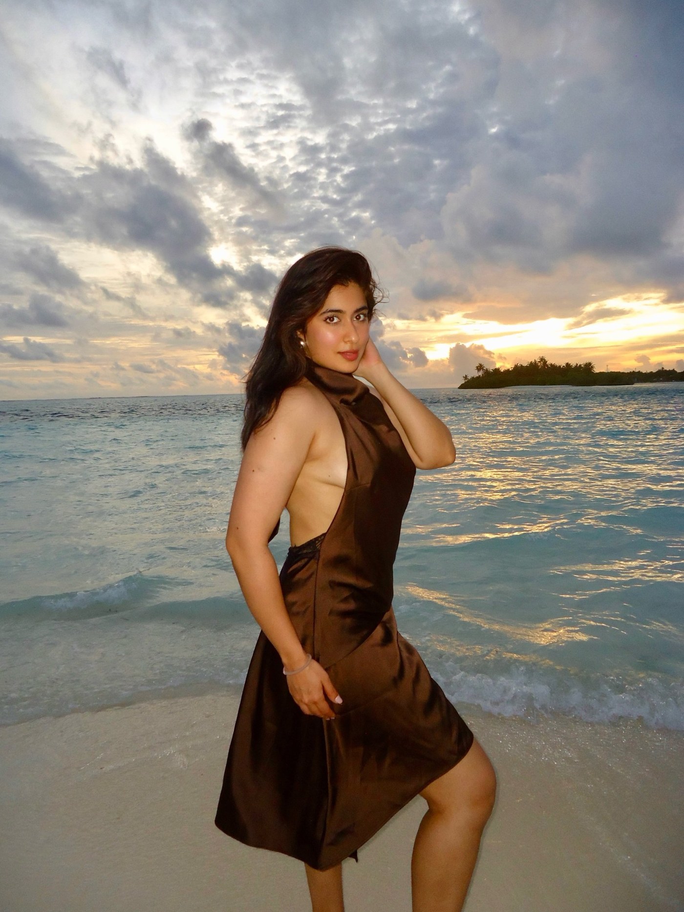 Nikita Sharma radiates soft confidence in a flowing ensemble against a stunning seaside sunset backdrop.