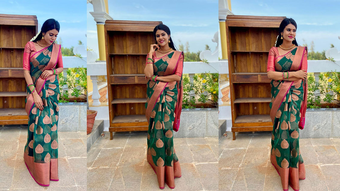Nivisha posing outdoors in a richly patterned emerald green and coral sari, showcasing elegant traditional wear.