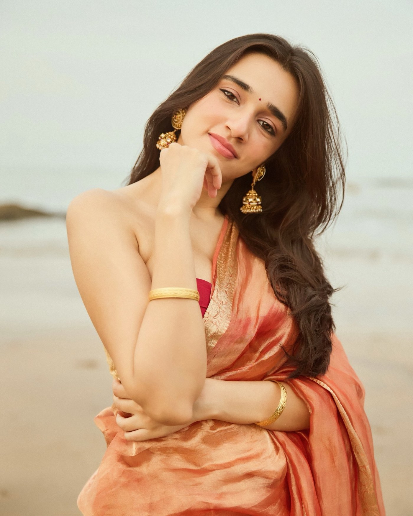 Nuveksha shines in a luxurious copper-gold saree against a breathtaking natural backdrop.