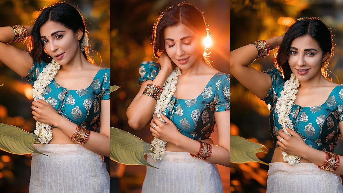 Parvati Nair in a close-up portrait bathed in warm, golden light, wearing teal embroidered attire and adorned with a flower garland.