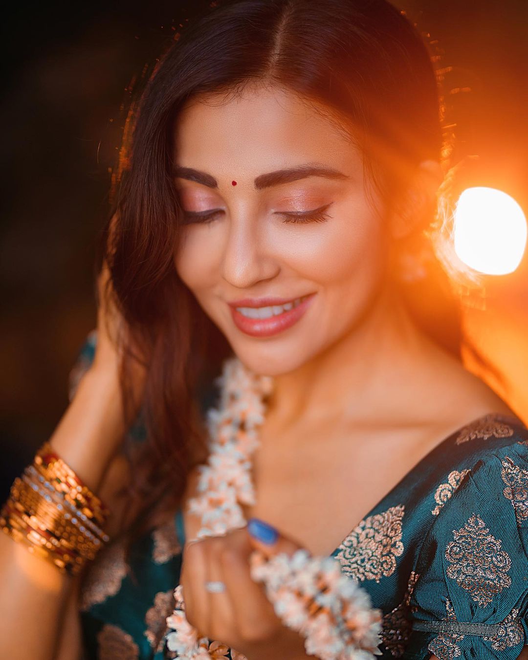 Parvati Nair in a close-up portrait bathed in warm, golden light, wearing teal embroidered attire and adorned with a flower garland.