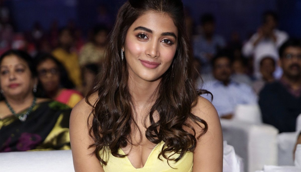 Pooja Hegde posing in a shimmering yellow strapless dress against a vibrant red and gold background with voluminous hair.
