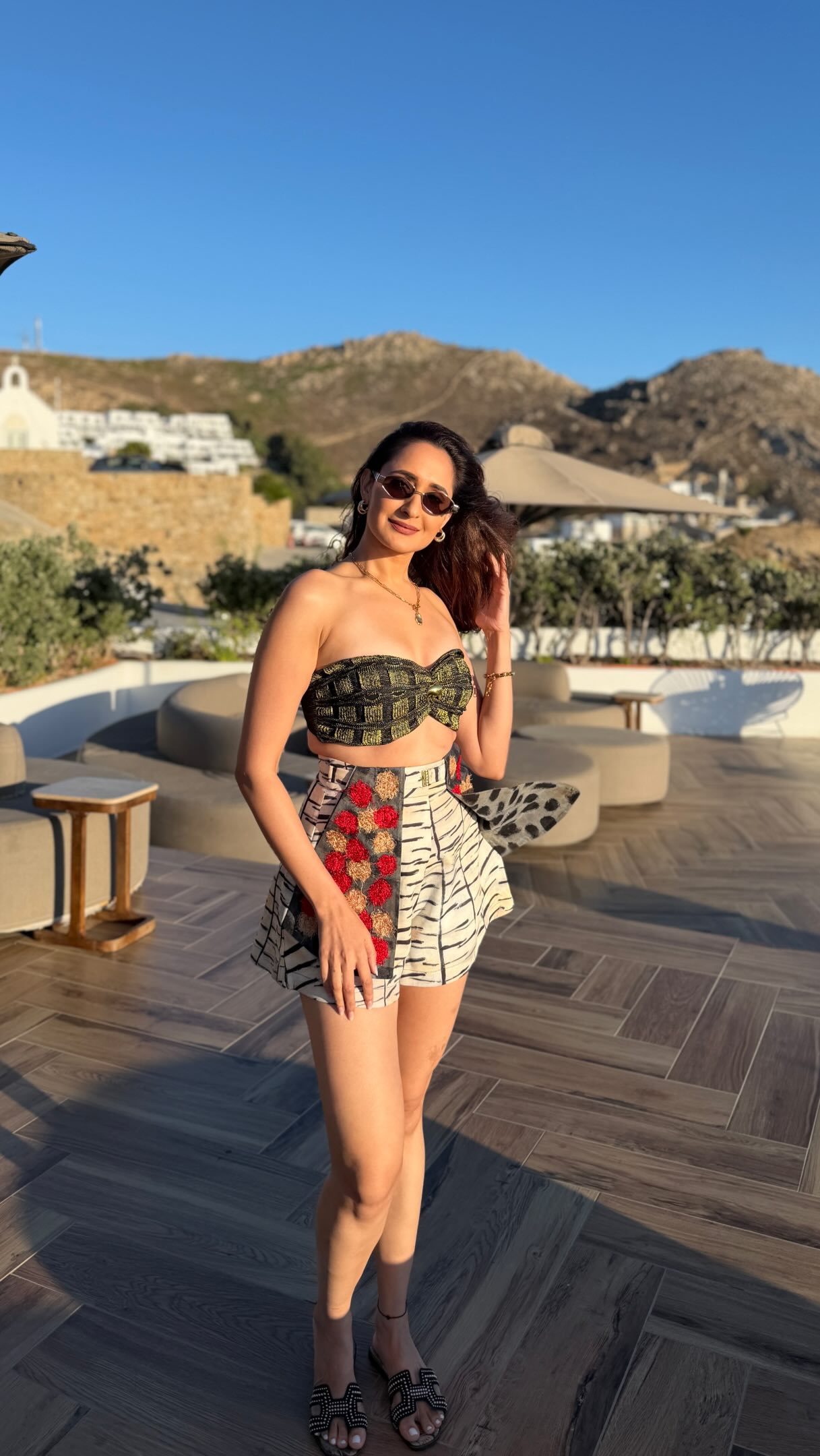 Pragya Jaiswal poses in a textured black top and colorful printed shorts against the whitewashed backdrop of Mykonos.