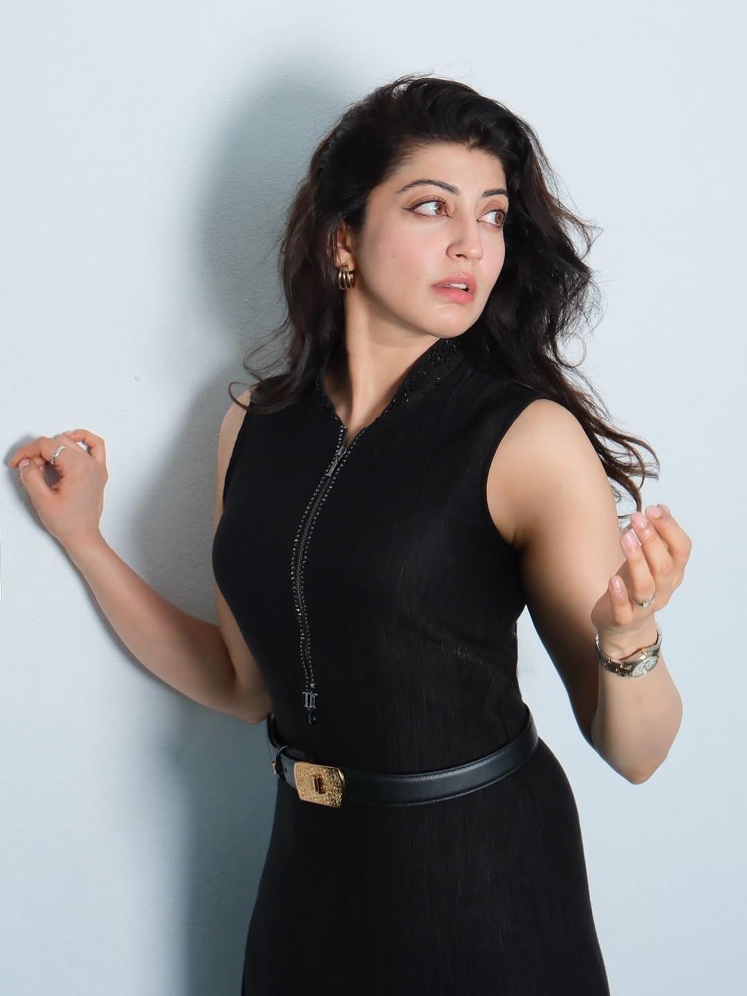 Pranitha Subhash posing in a black garment with a gold belt and ornate buckle against a light background.