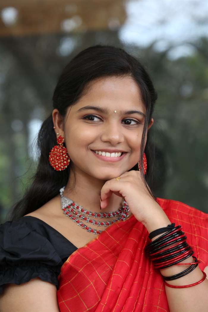 Prarthana Sandeep in an olive green patterned top with a reddish-maroon bracelet, standing in a warmly toned outdoor setting.