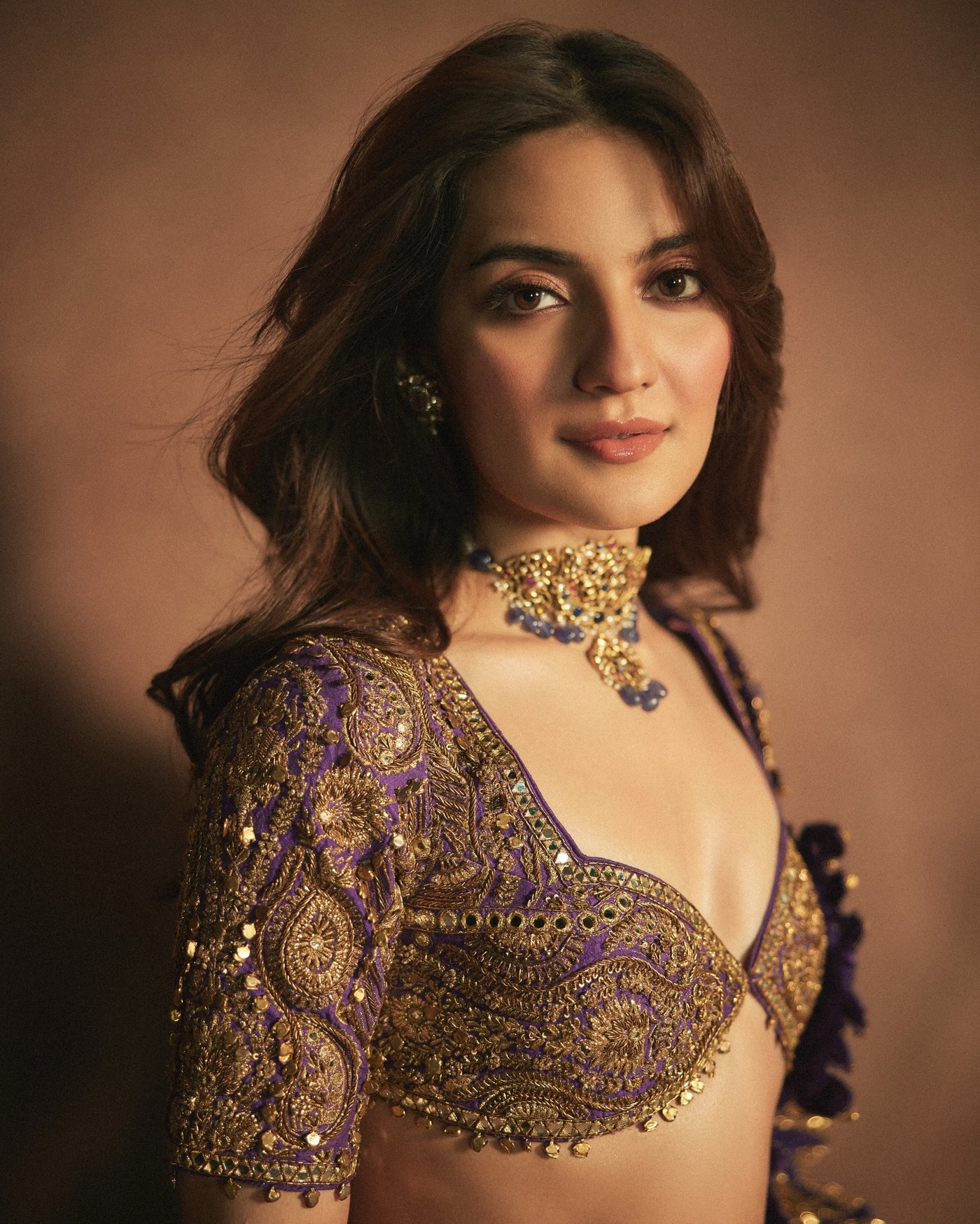Pratibha Ranta posing in a heavily embellished lehenga choli against a warm brown background.
