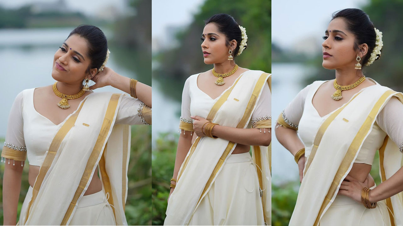 Rashmi Gautam wearing a cream and gold draped outfit with gold jewelry and white flowers in a natural setting.