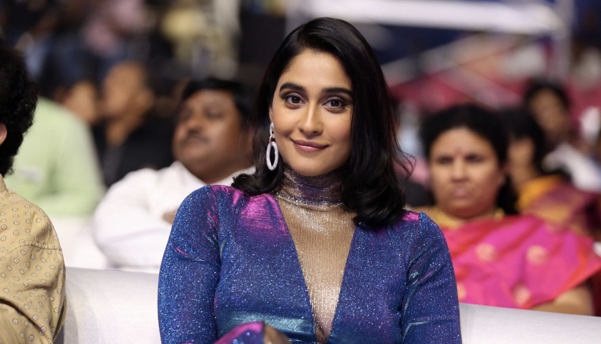 Regina Cassandra stands on a red carpet wearing a shimmering blue and purple gown with statement earrings.