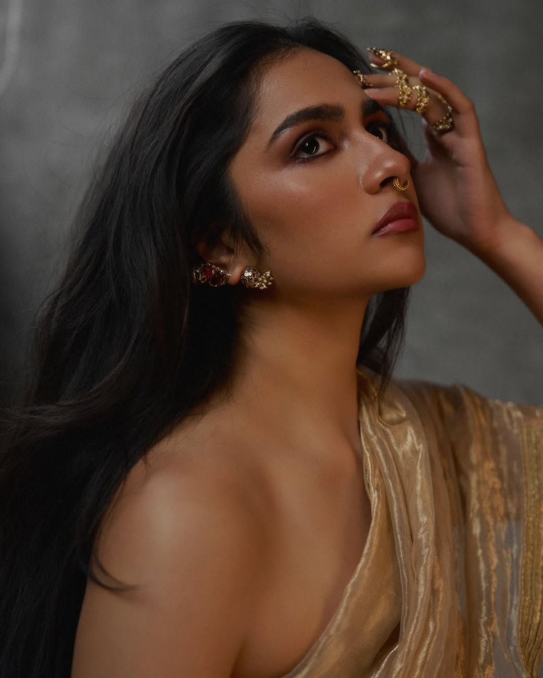 Rukmini Vasanth in a draped golden fabric with gold jewelry and long dark hair.