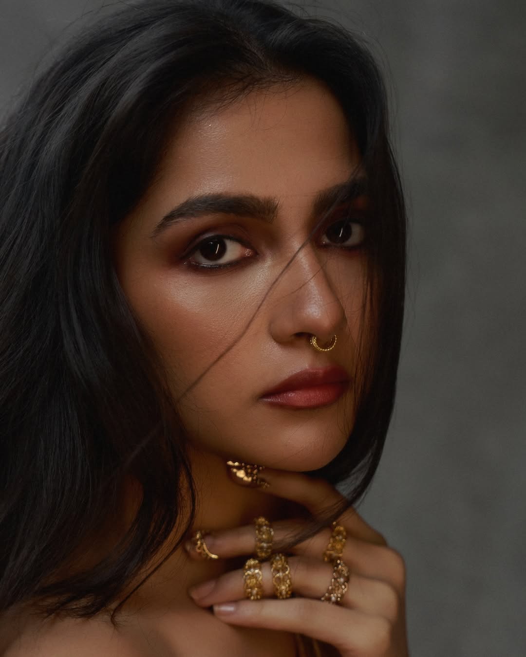 Rukmini Vasanth in a close-up portrait with gold accessories and flowing dark hair, set against a dark background.