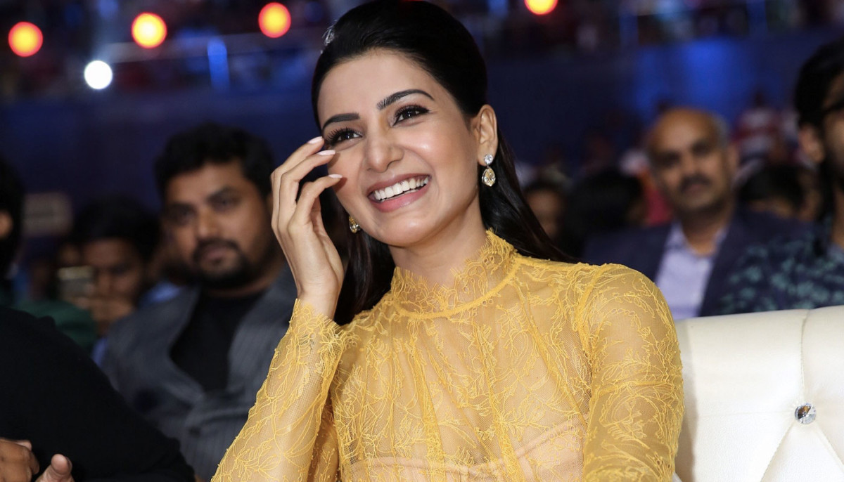 Samantha Akkineni is seated on a light-colored, tufted sofa wearing a vibrant, bright yellow ensemble.
