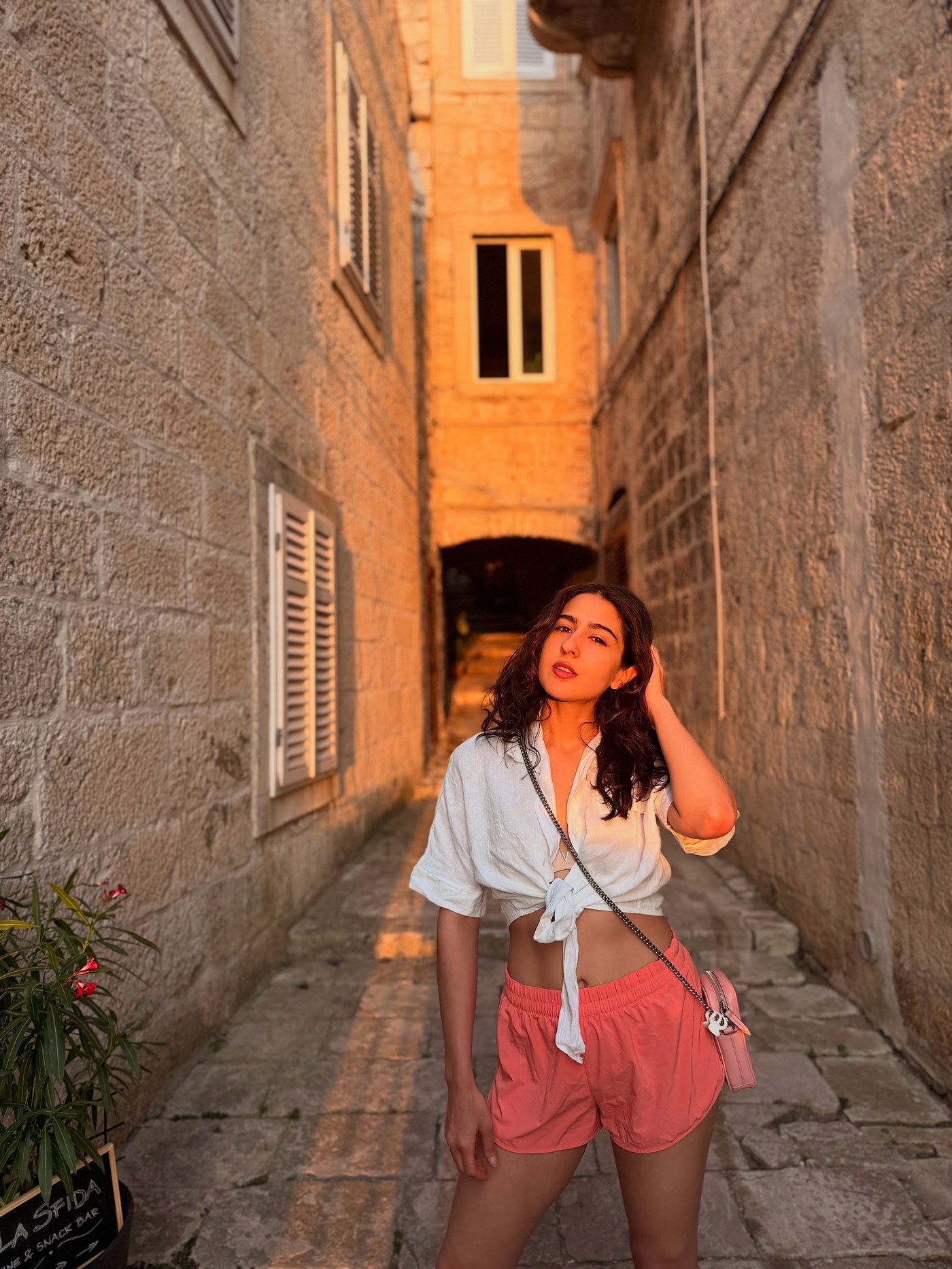 Sara Ali Khan radiates effortless glamour in a knotted white shirt and vibrant coral shorts.