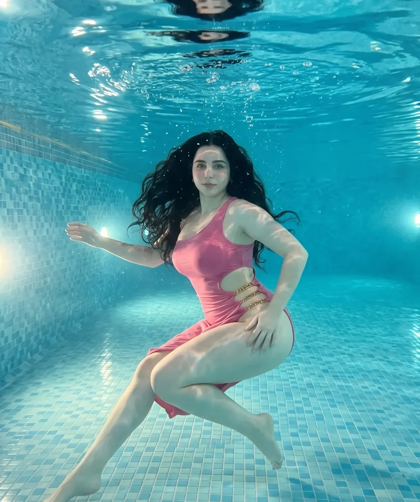 Maaya in a vivid pink, flowing dress within a blue pool setting. - Photos & Updates