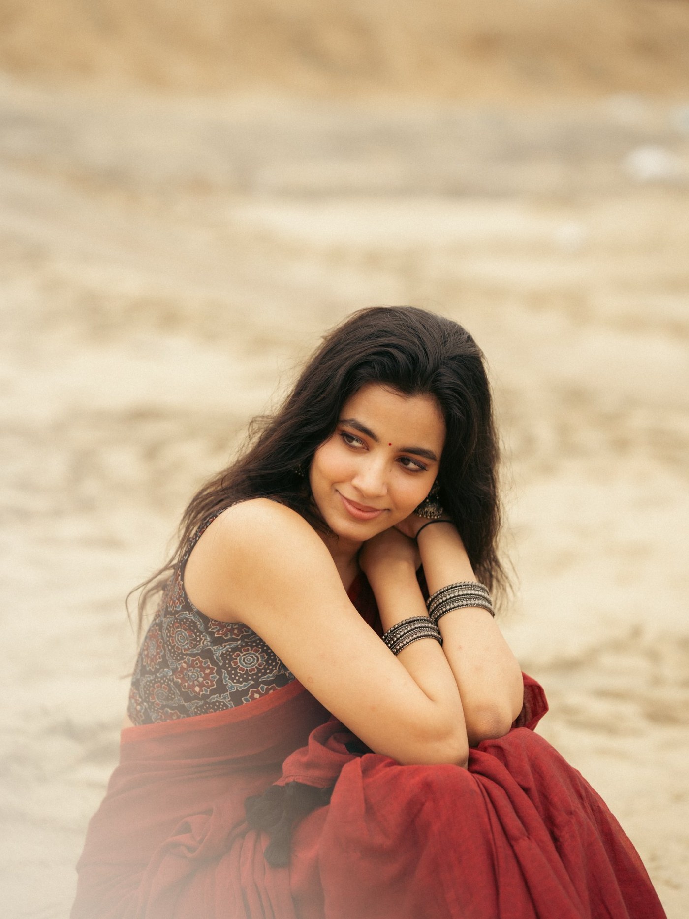 Shivani Nagaram poses gracefully in a vibrant red saree against the serene backdrop of the beach.