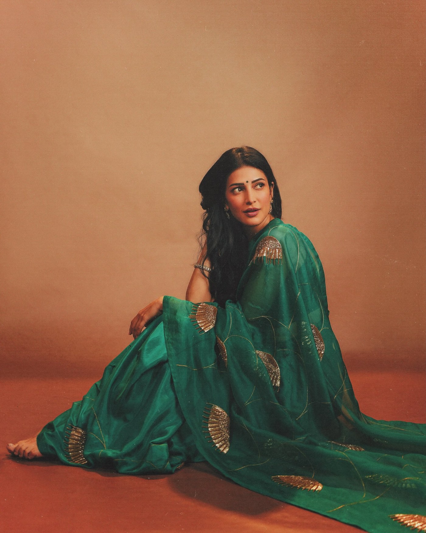 Shruti Haasan is seen in a deep emerald green saree with gold detailing, striking a poised three-quarter profile against a soft studio backdrop. - Photos & Updates