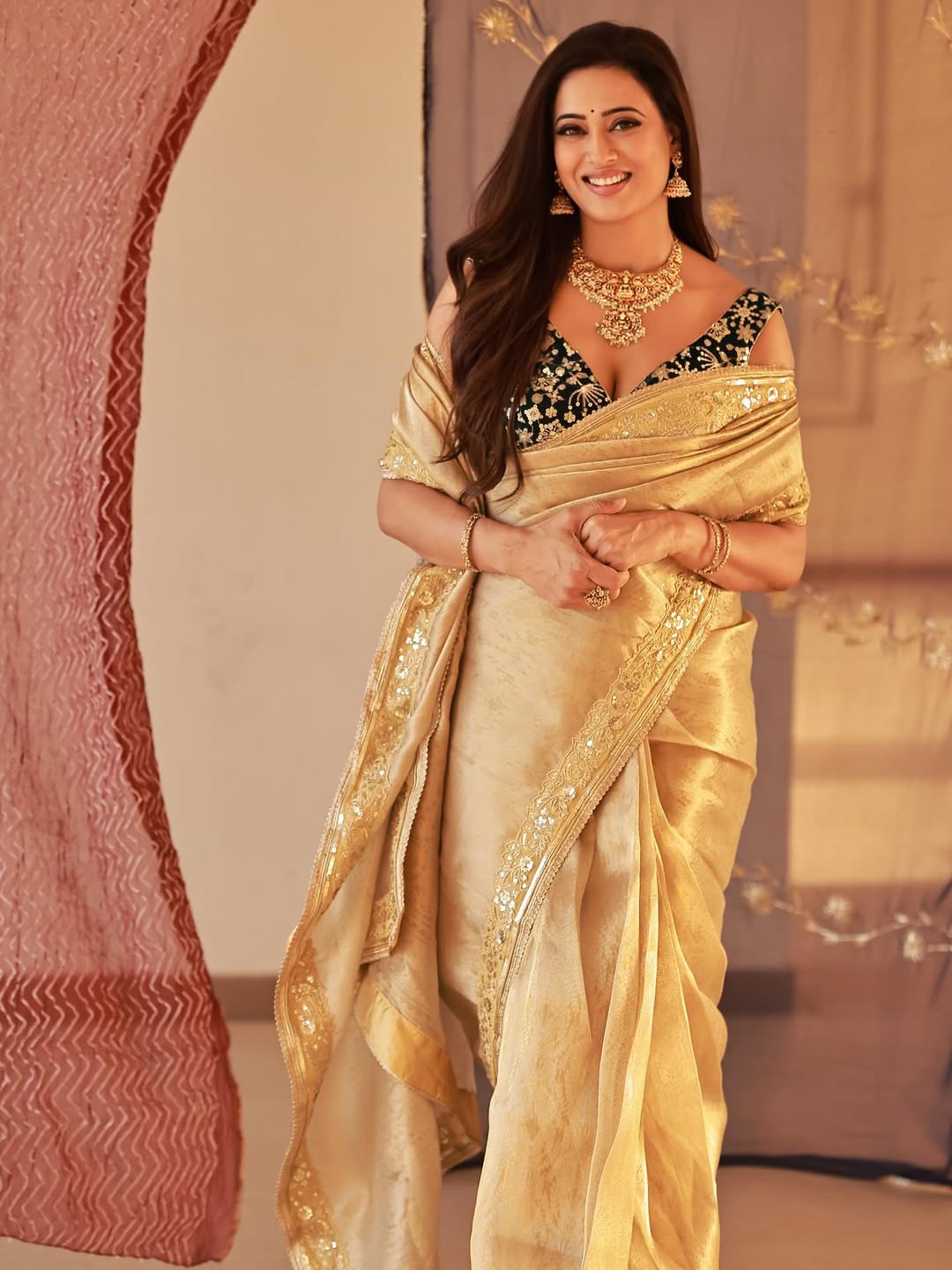Shweta Tiwari is wearing a traditional golden saree with heavy gold jewelry and long, dark hair.
