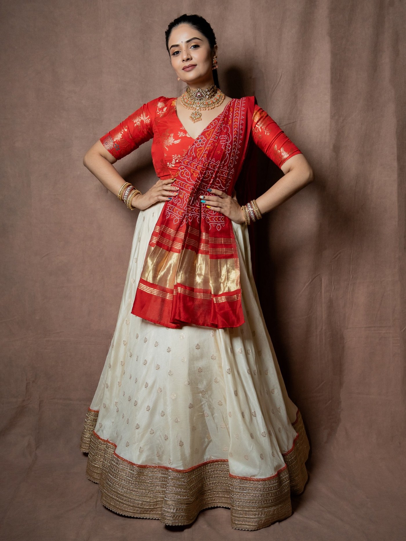 Sreemukhi shines in a vibrant red and cream ensemble, showcasing intricate gold embroidery and traditional jewelry.