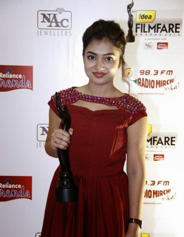 The subject is posing with another woman at an indoor event, smiling warmly, wearing a dark necklace and a ring.