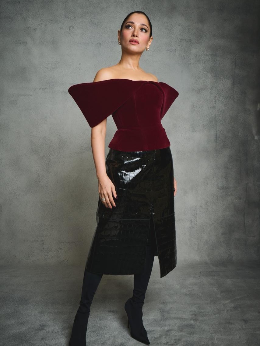 Tamannaah Bhatia posing in a high-waisted black patent outfit against a solid gray background.
