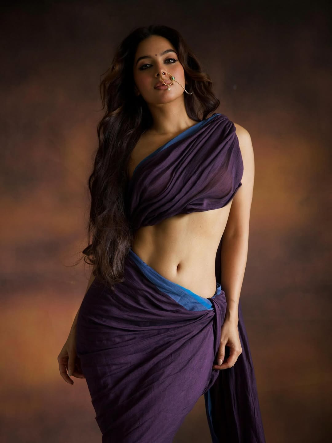 Tanya Hope leaning on a dark wooden surface near a window, wearing a textured, light-colored knitted garment.