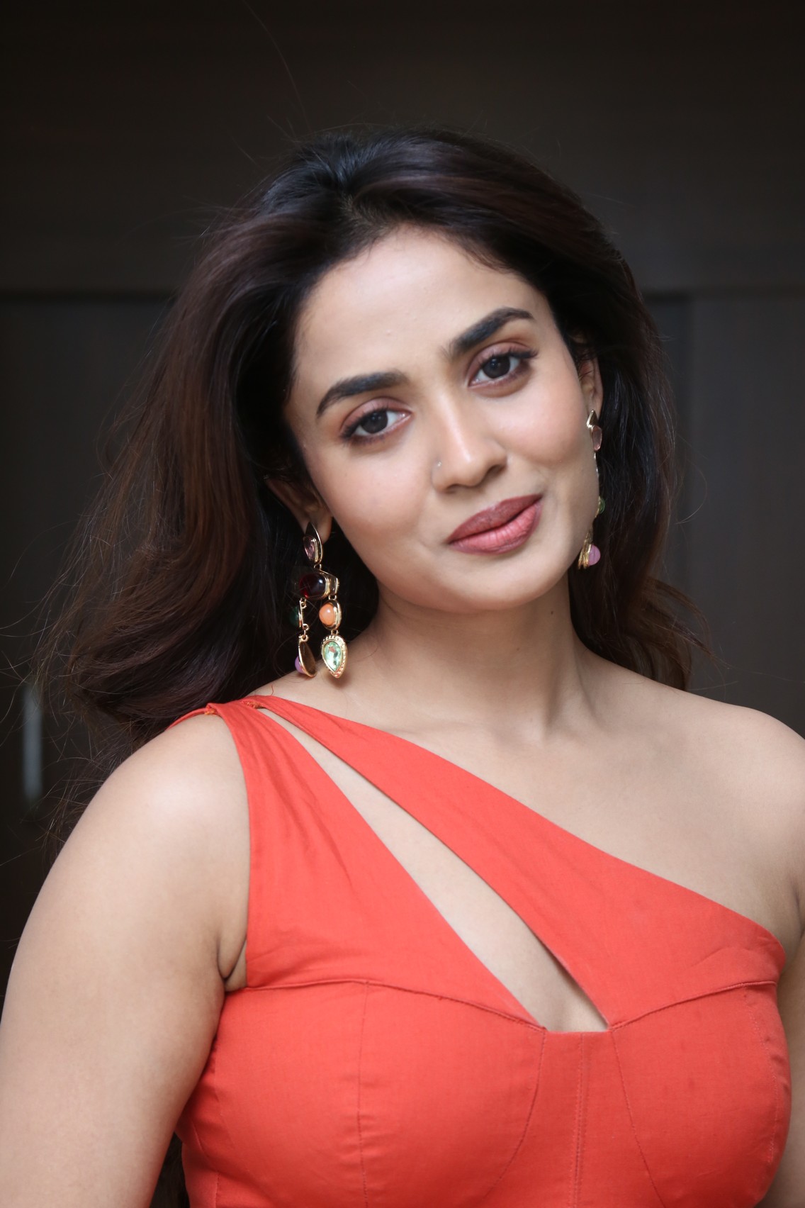 Teju Ashwini posing in a vibrant reddish-orange outfit against a plain white background.